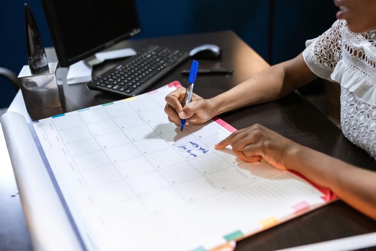 Hands marking dates on a large desk calendar