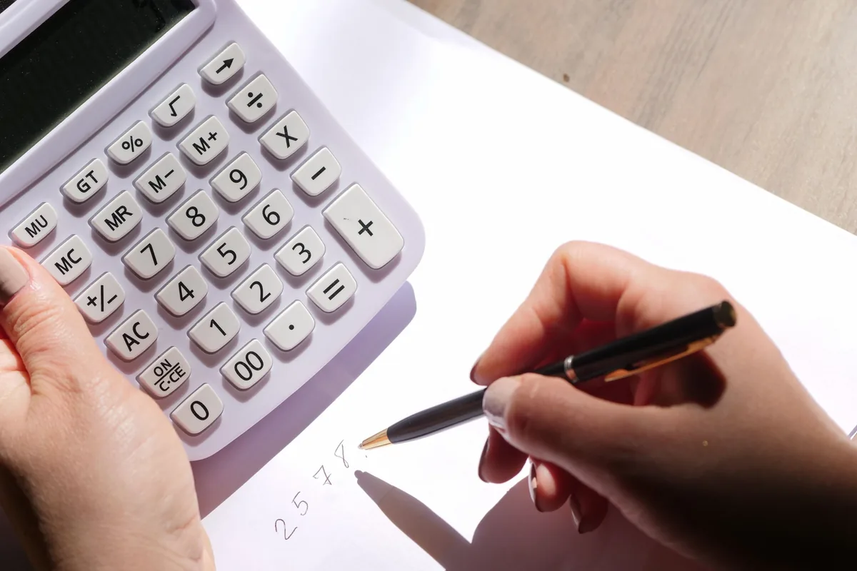 Hands using a calculator while writing figures on paper