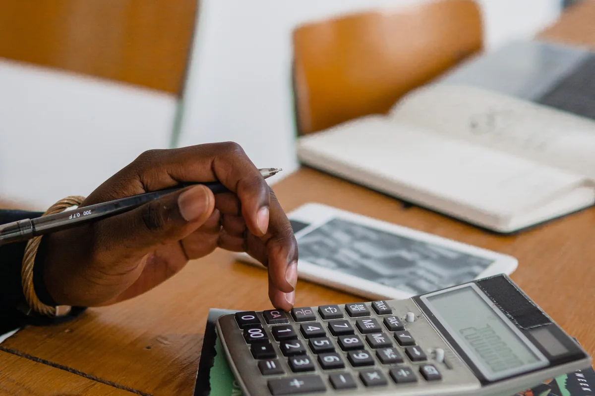 Hand using a calculator at a desk with books and a notebook