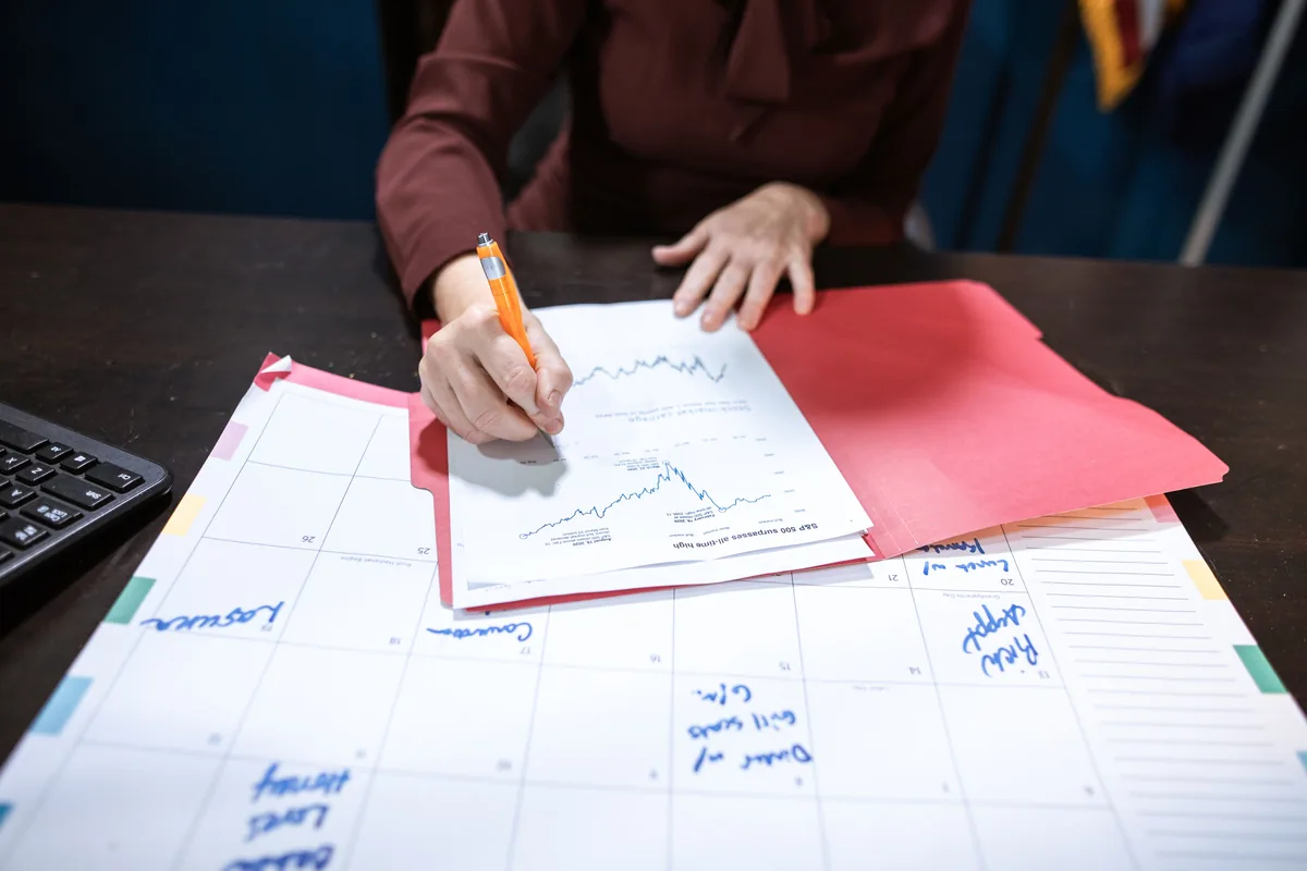 Hands writing on a financial chart above a large planning calendar
