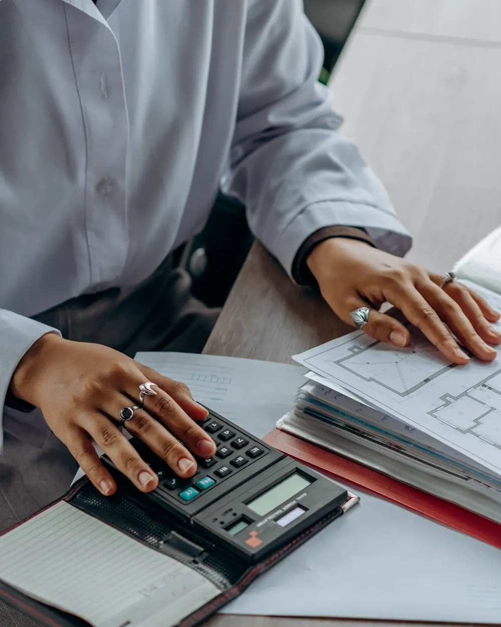 Hands using a calculator beside property plans and organized records