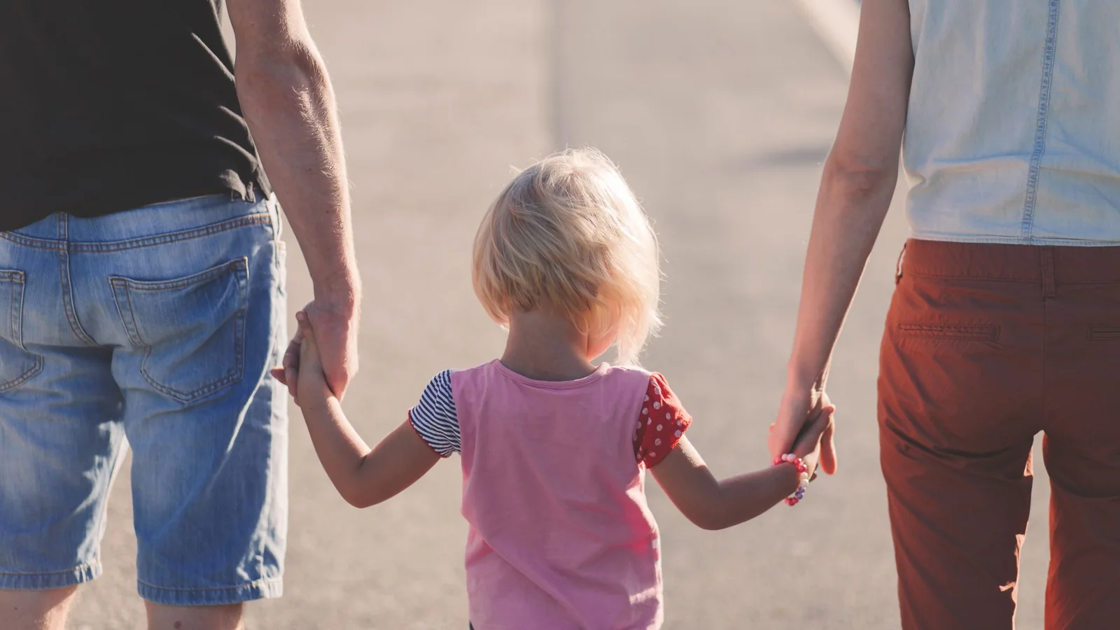 A child walking between two parents and holding both of their hands